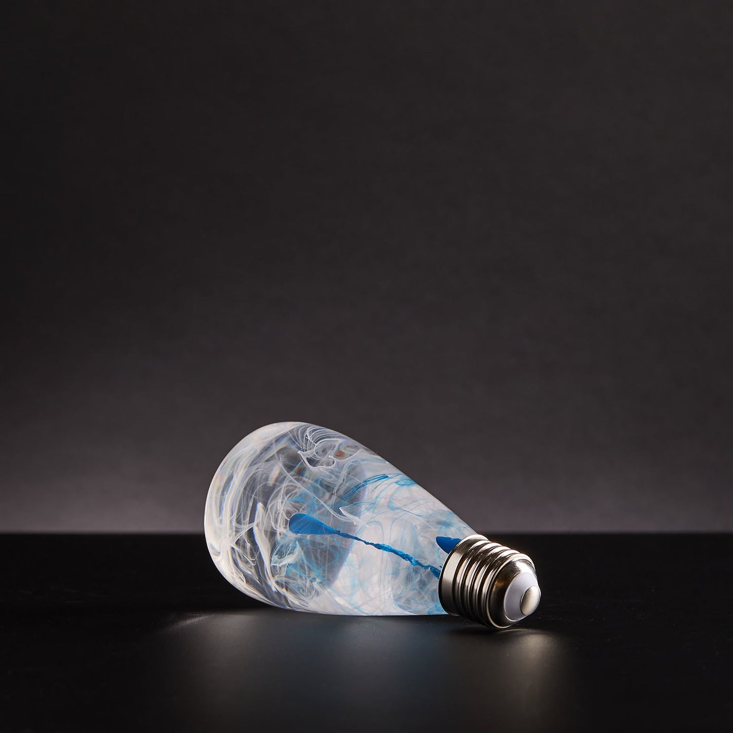 Decorative light bulb with blue and white ink drop swirl inside laying on its side.