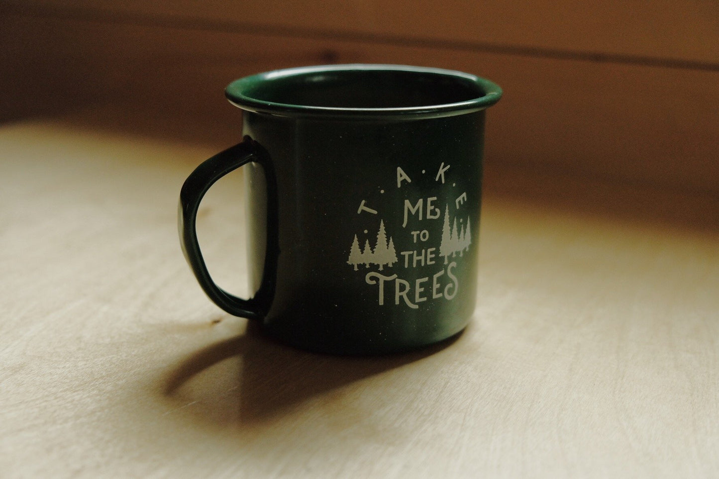 12 ounce Green enamel mug, printed in white with graphic that says, “Take me to the trees” and evergreen drawings.