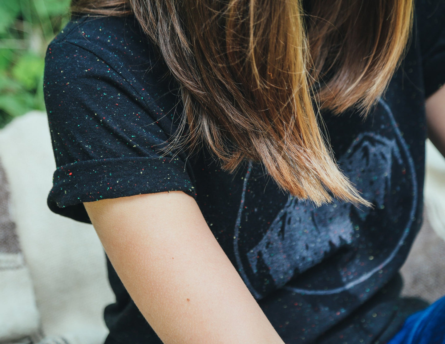 Close up of woman wearing black with white speckle tee shirt featuring moonrise over mountain range graphic.