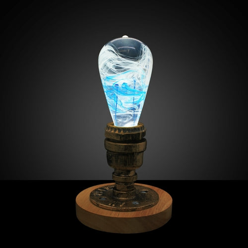 Lit decorative light bulb with blue and white ink drop swirl inside, screwed into a vintage style brass and wood base.