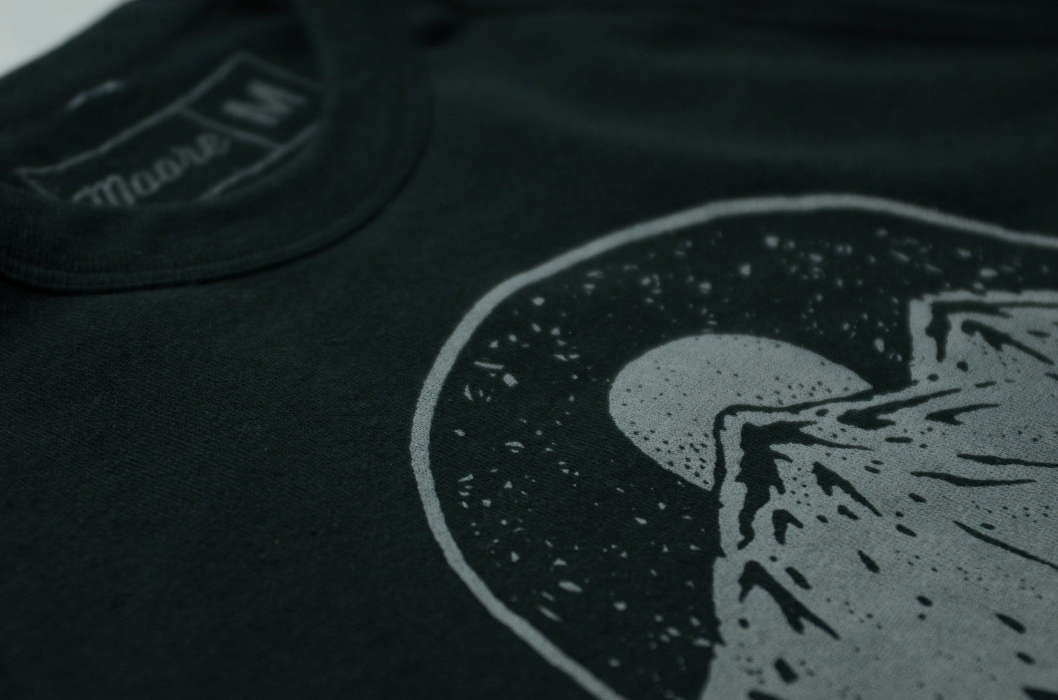 Close up of printed moonrise over mountain range graphic on the front of a black unisex sweatshirt.