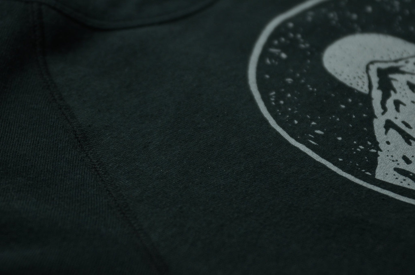 Close up of printing and seams on black unisex crew neck sweatshirt, featuring moonrise over mountains graphic.