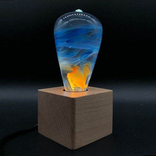 Clear lightbulb with orange, yellow, and blue swirls set in wooden base in dark room.