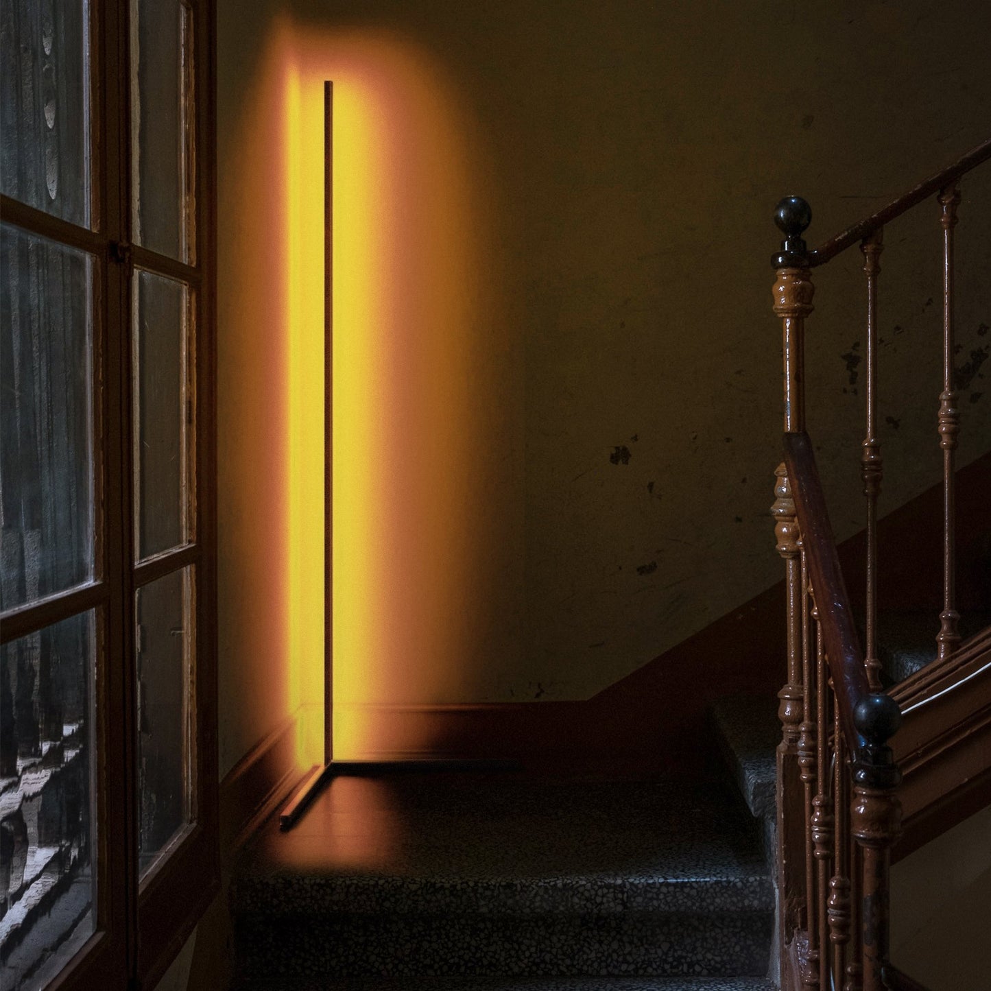 Minimalist Corner RGB floor lamp, lit with warm yellow orange lights, illuminating corner of a staircase.