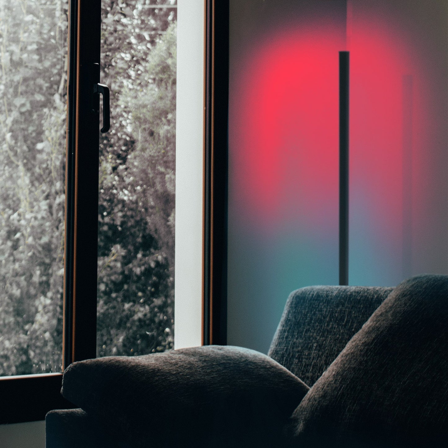 Minimalist Corner RGB floor lamp, lit with blue and red lights, illuminating corner of a living room behind a couch.