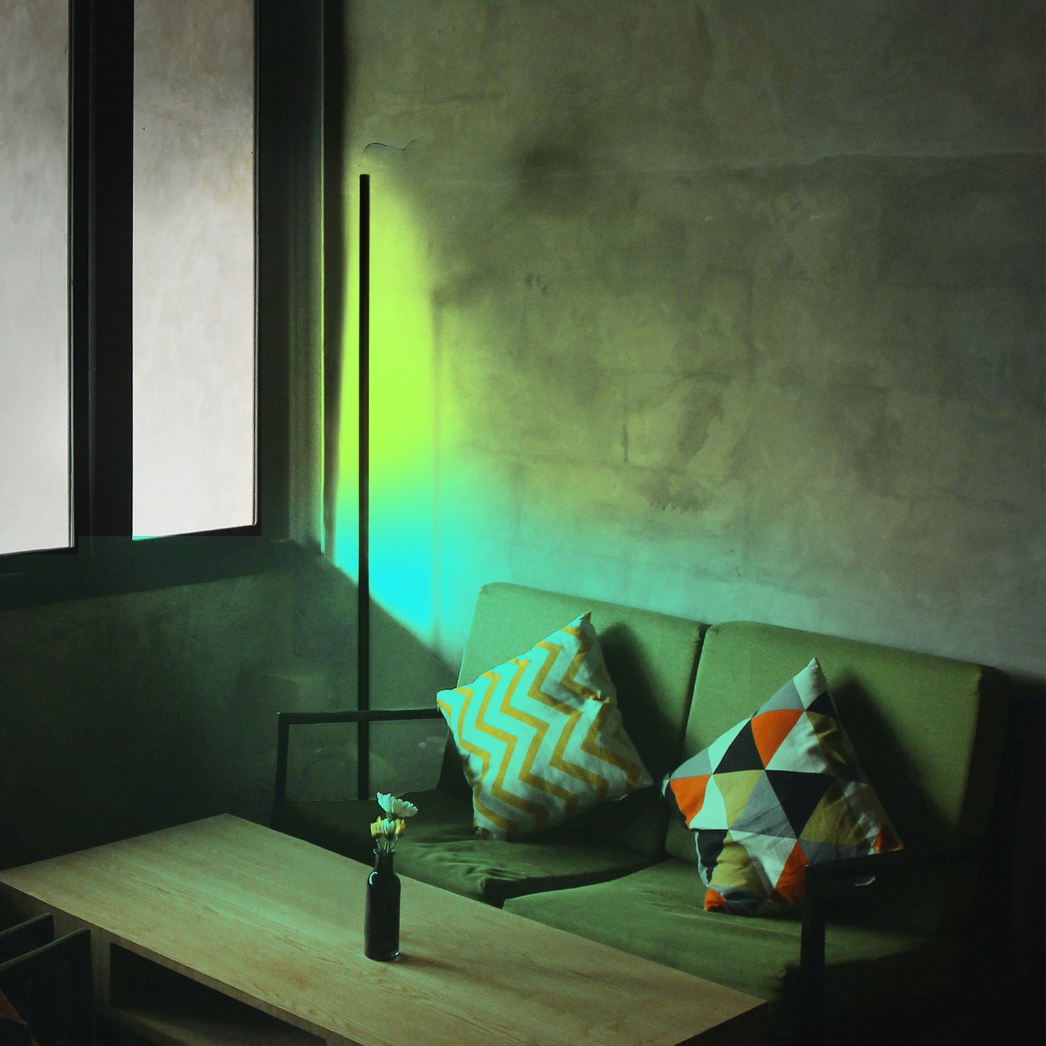 Minimalist Corner RGB floor lamp, lit with blue, yellow, and green lights illuminating corner of a living room behind a couch.