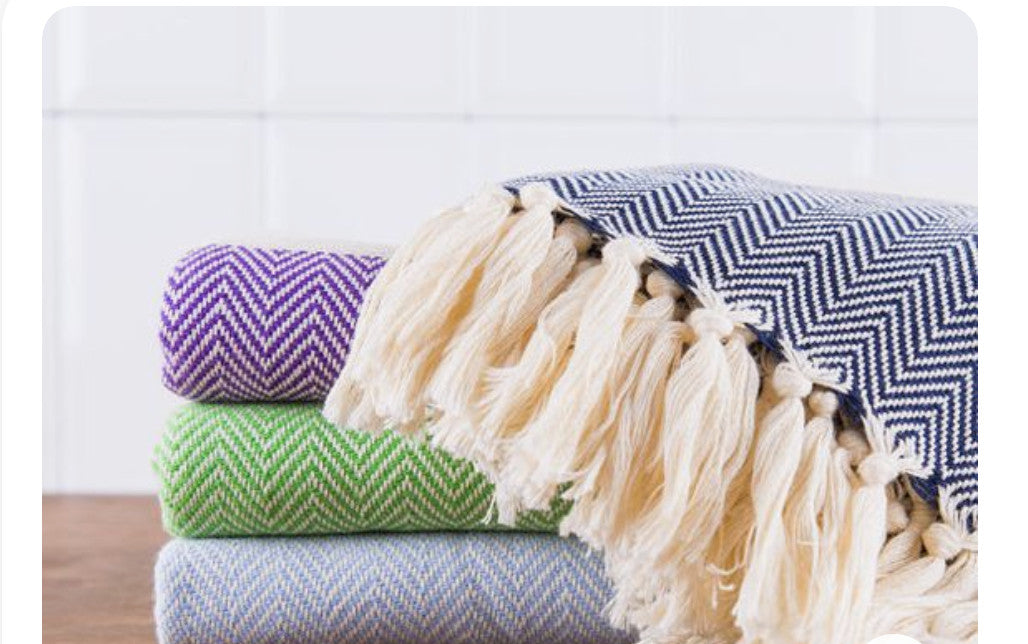 Stack of multiple colors of neatly folded Turkish hand towels atop wood surface with close view of off-white tassels.