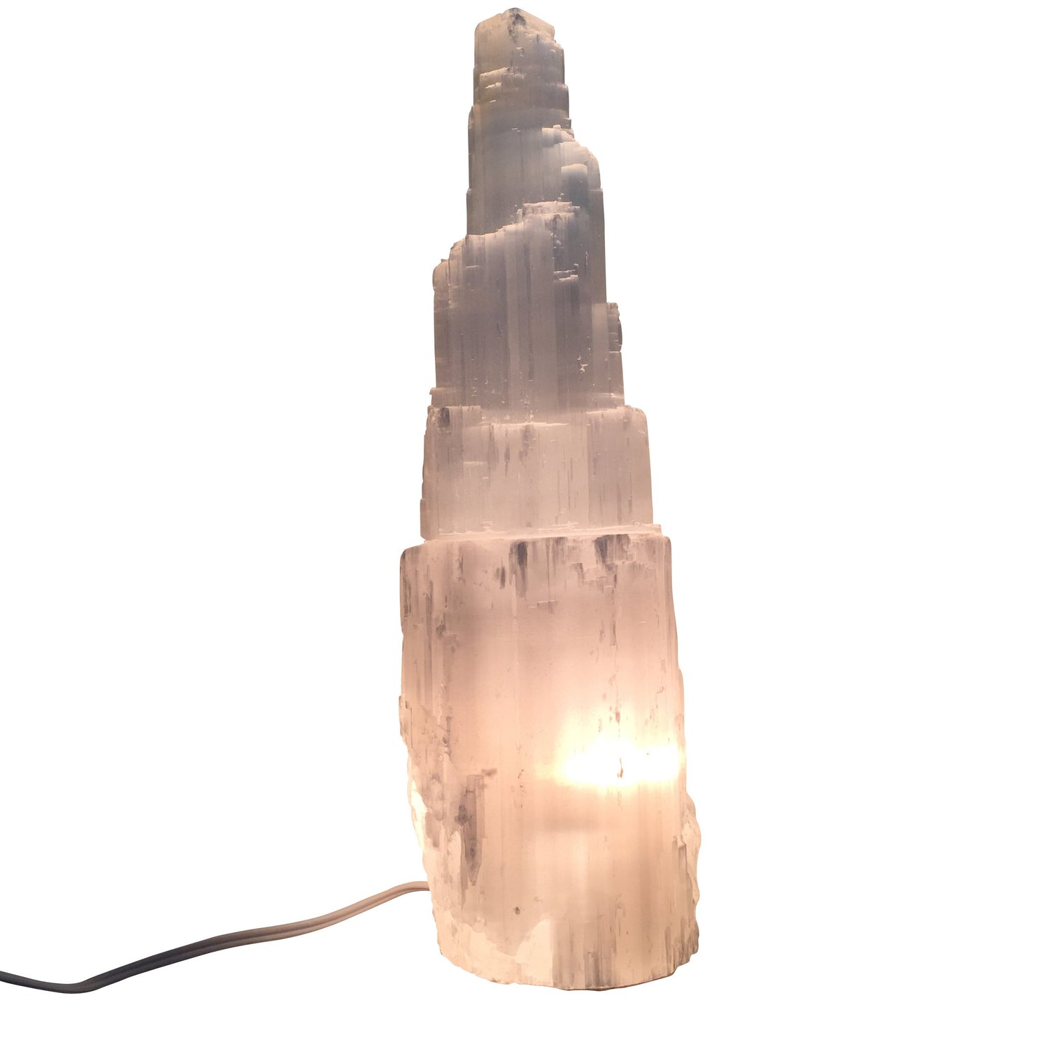 Selenite crystal tower illuminated from light within, with black cord visible on all white background.