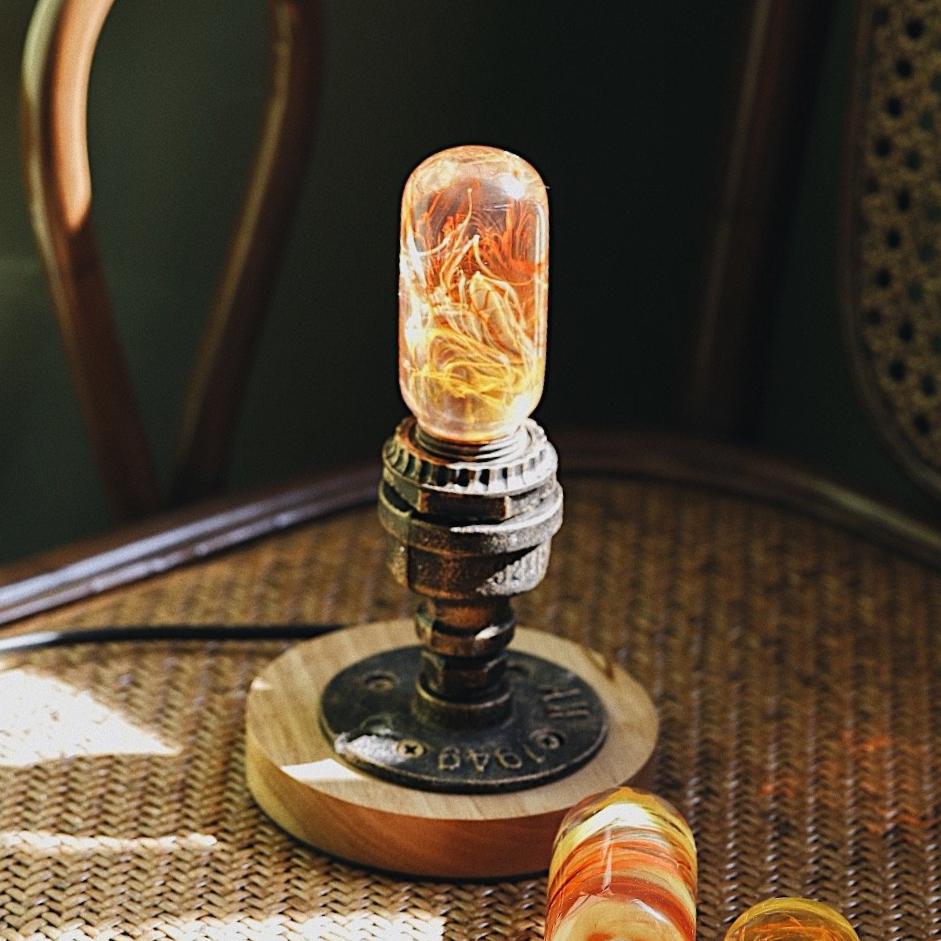 Oval decorative resin bulb with orange and yellow flame like streaks inside, sits unlit atop vintage brass pipe and wood base, unlit.