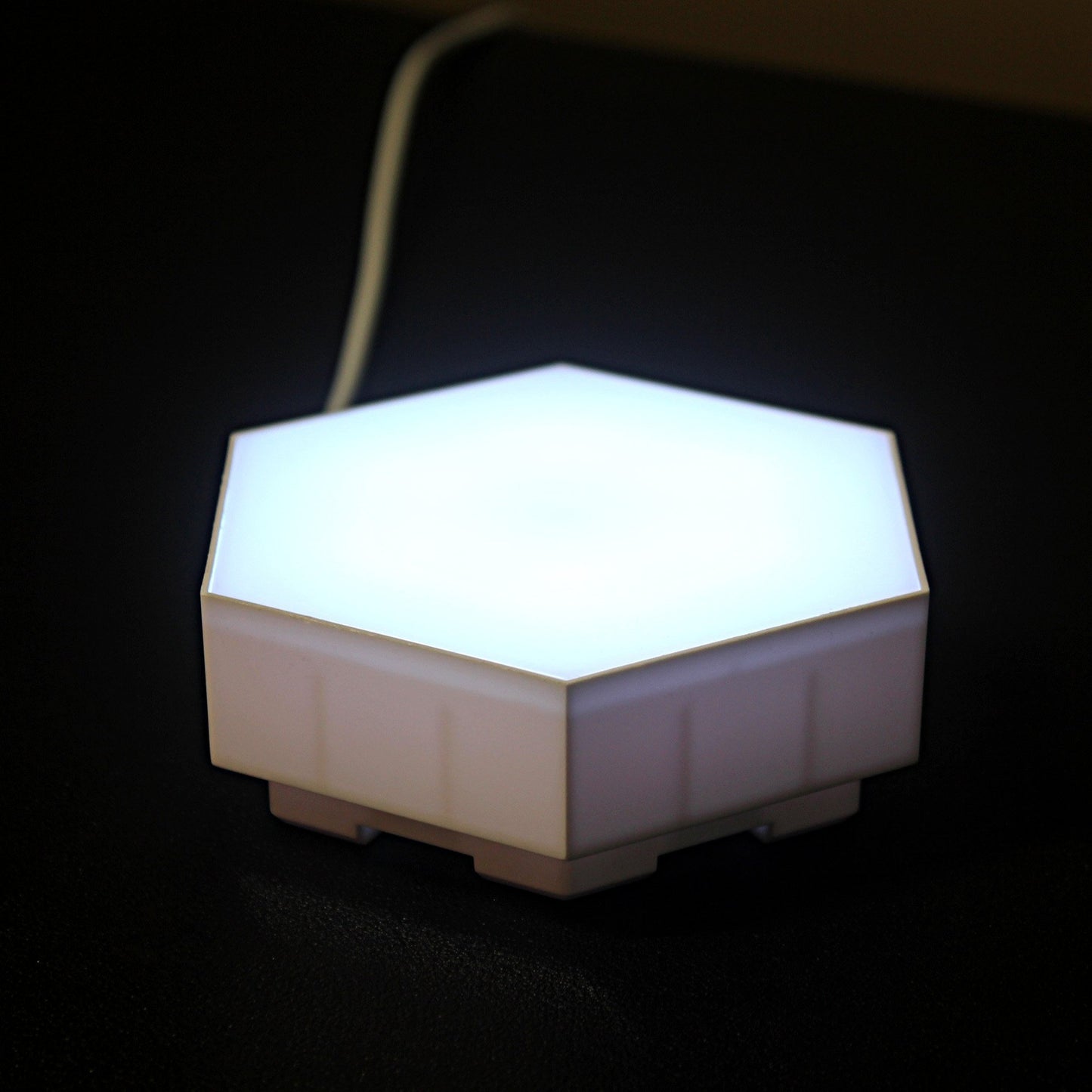 Single module of Touch Sensitive Honeycomb Modular Wall Lights shown lit in white on a table top from the side to show depth. 