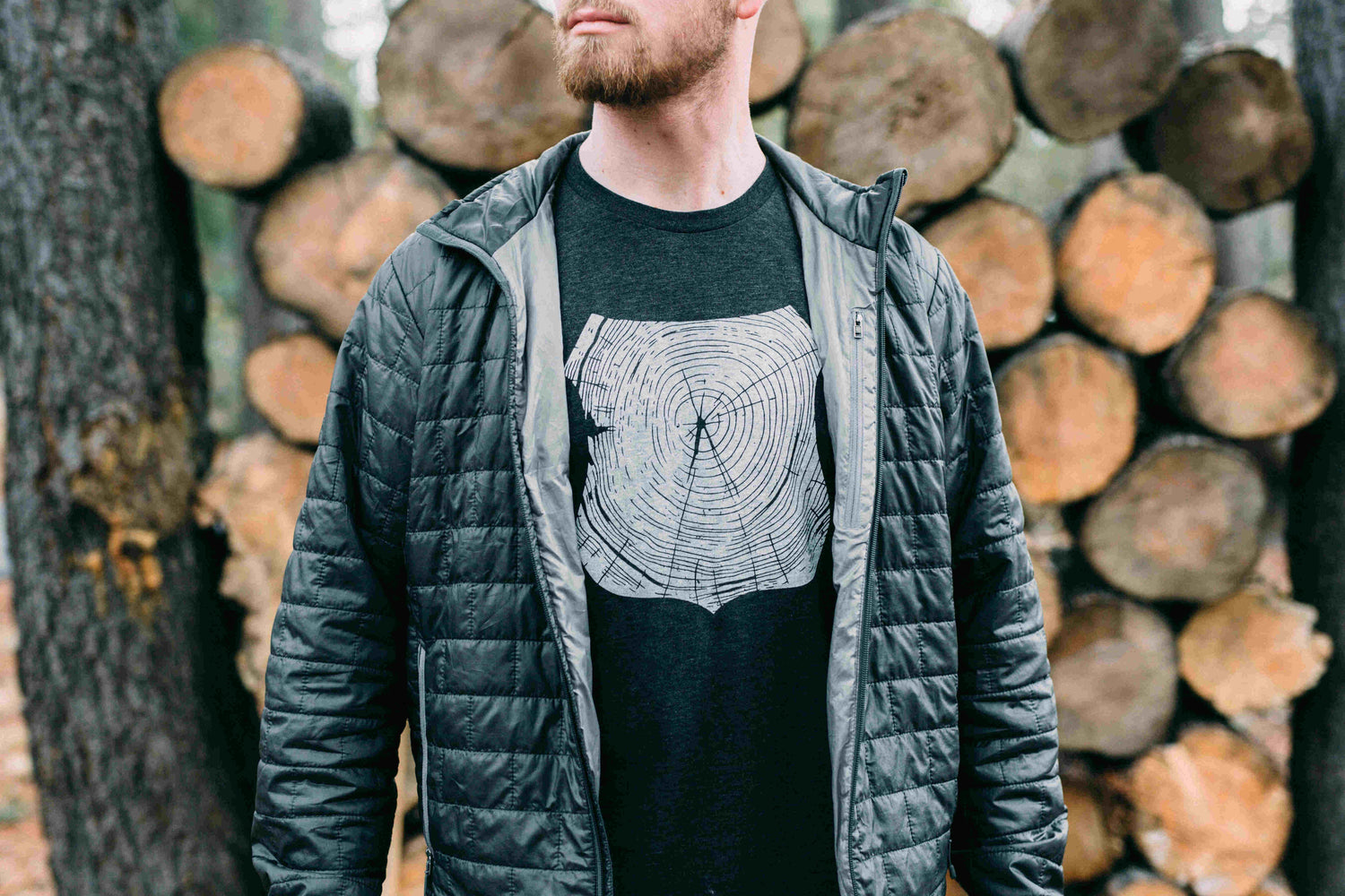 Man wearing gray tee shirt printed with white forest ranger badge outline, filled with tree rings. 