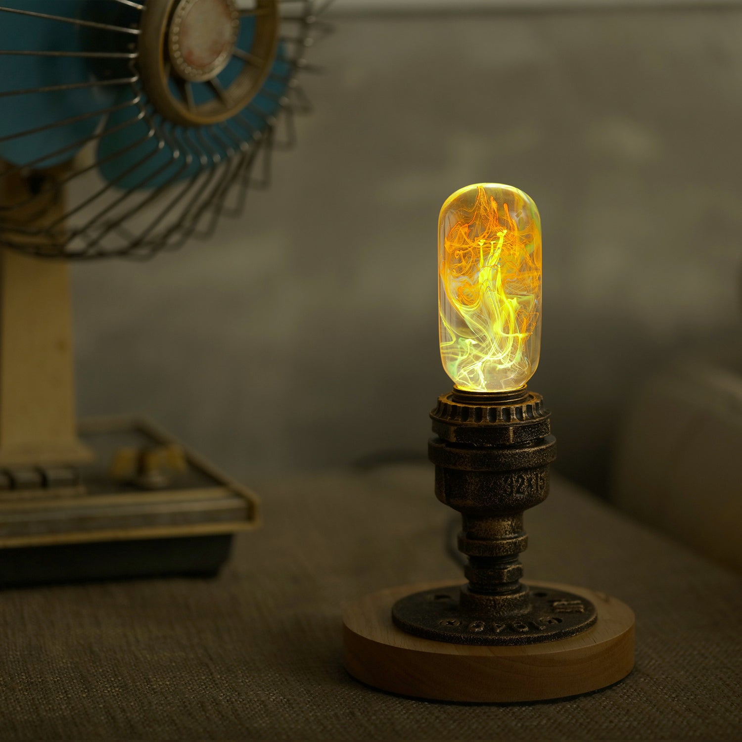 Oval decorative resin bulb with orange and yellow flame like streaks inside, sits lit atop vintage brass pipe and wood base.
