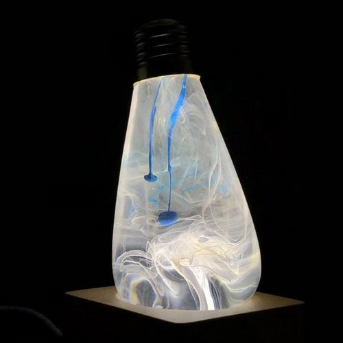 Decorative light bulb with blue and white ink drop swirl inside, upside down in wood base but lit to show smoke effect in bulb.