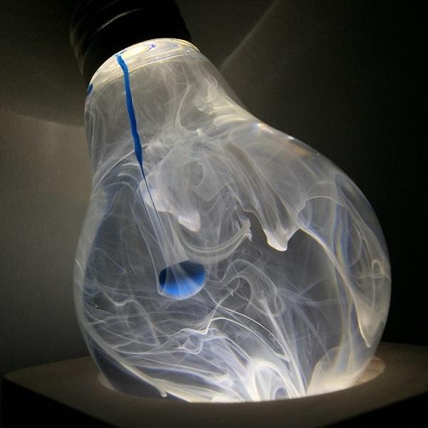 Decorative light bulb with blue and white ink drop swirl inside illuminated from the top to show smoke effect in bulb.