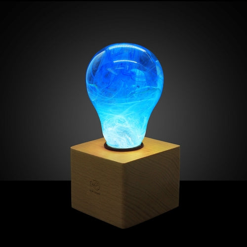 Illuminated clear lightbulb filled with blue swirls, set in wooden base in darkened room.