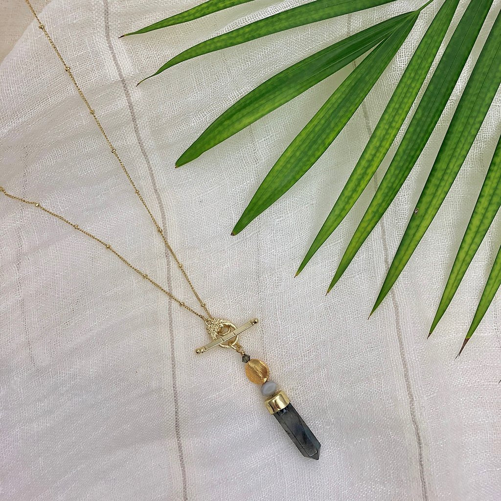 Necklace has a satellite chain with bar & circle closure, large labradorite pendant with glass bead. Shown on cloth backdrop.