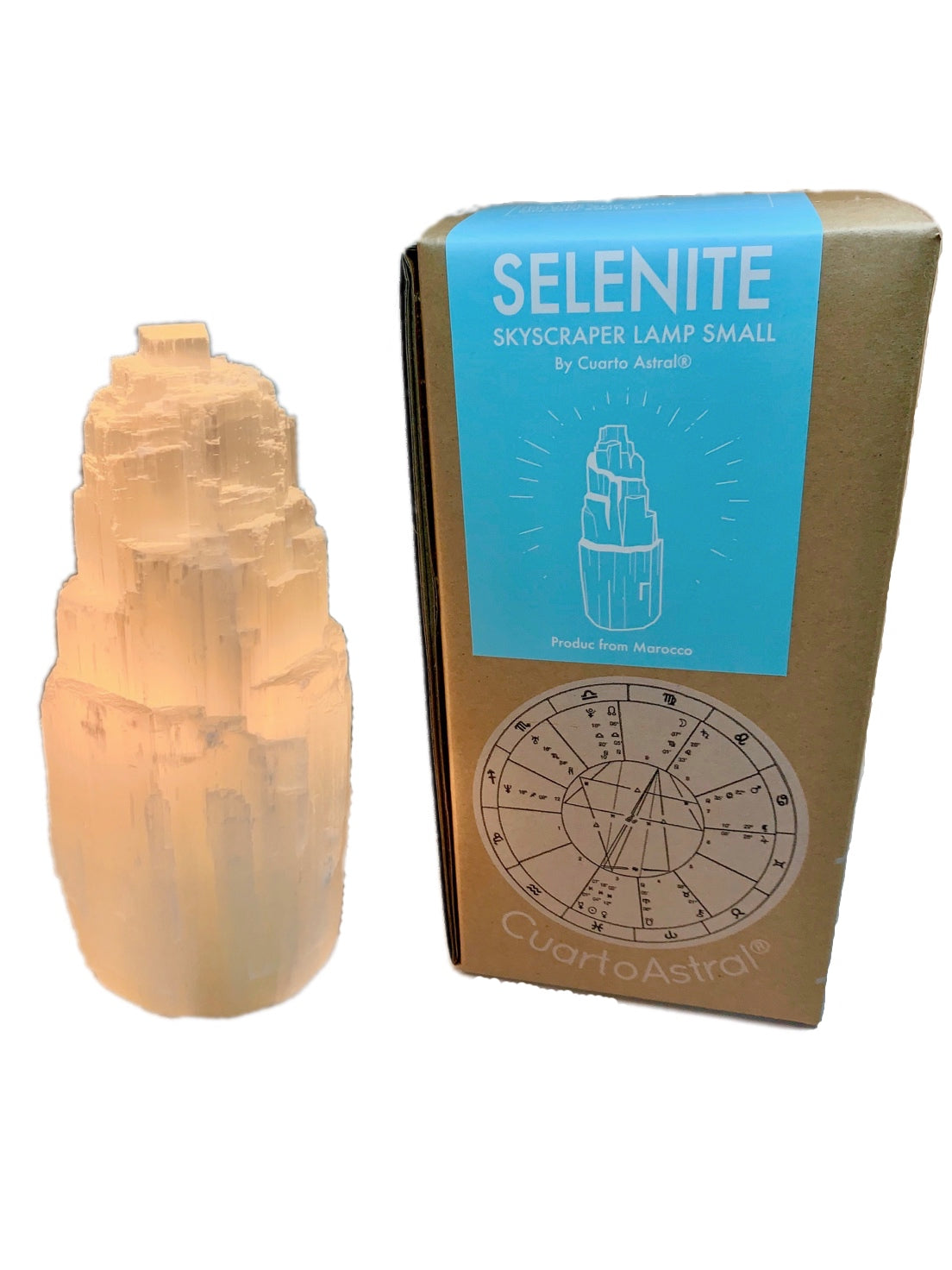 Small selenite skyscraper lamp, glowing from light within, beside with cardboard packing box from which it came.