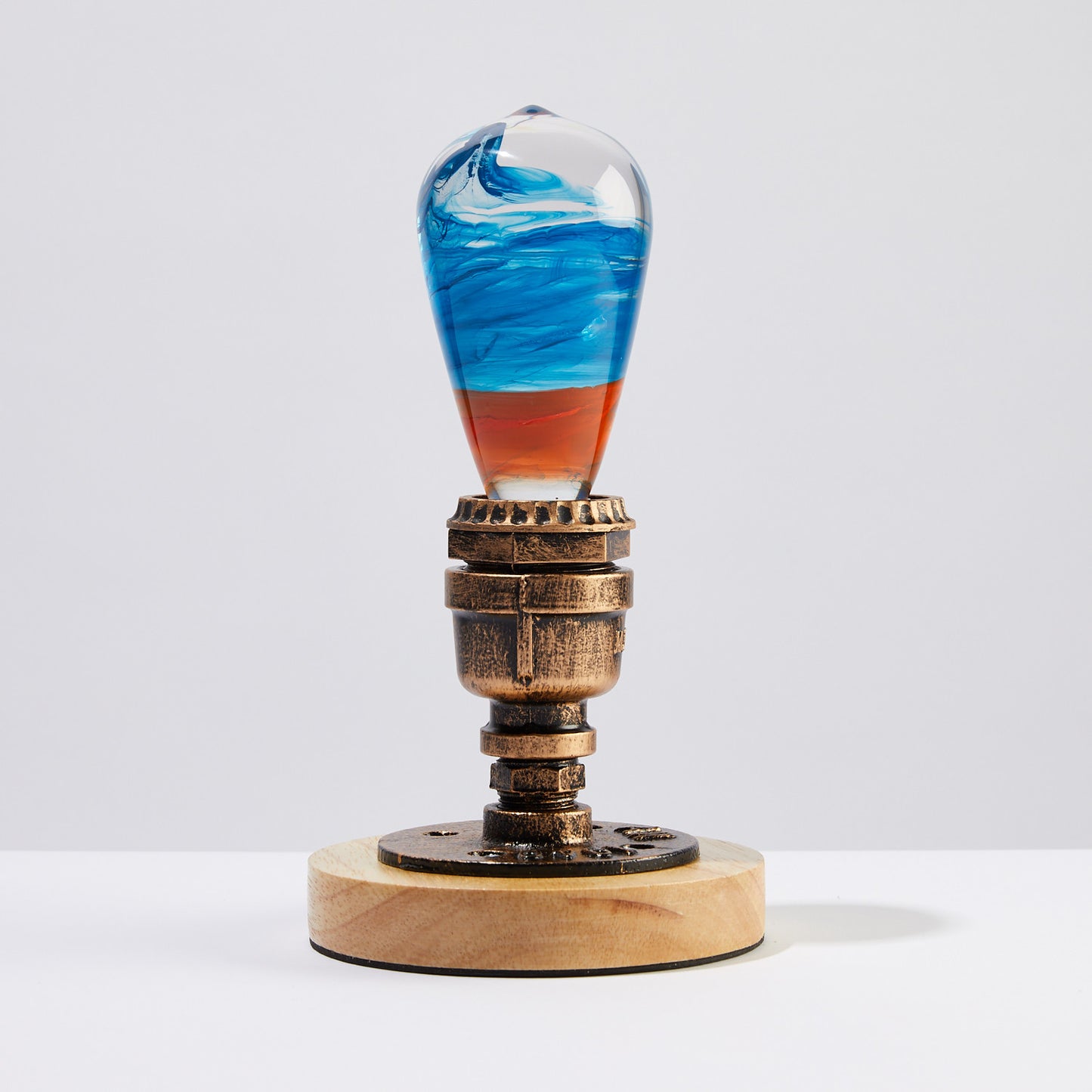 Clear lightbulb, filled with yellow, orange, red, and blue swirls, set in vintage copper and wood base in bright room.