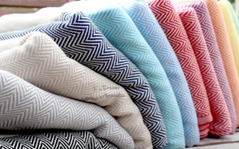 Folded towels in multiple colors of chevron patterning stacked atop a shelf in bright indoor space.