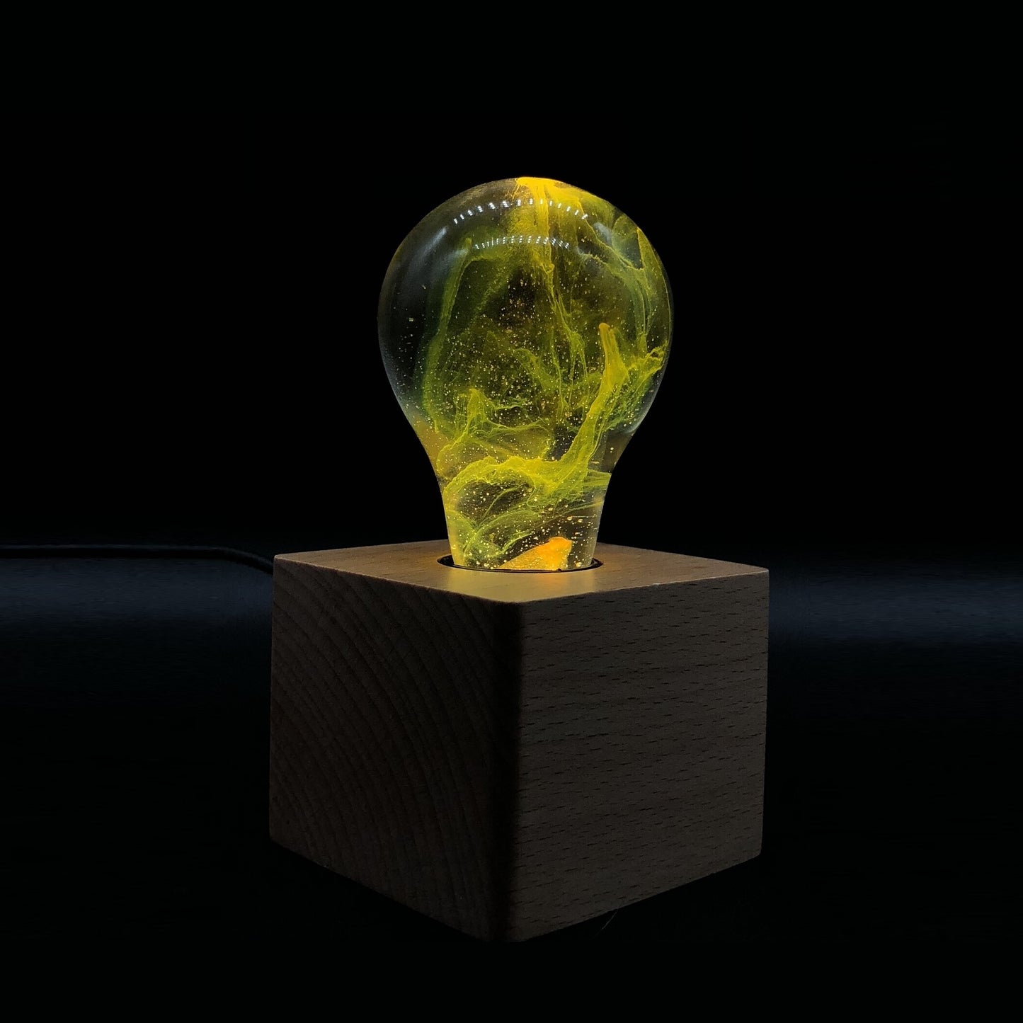 Clear lightbulb filled with yellow nebula clouds set in wooden base.