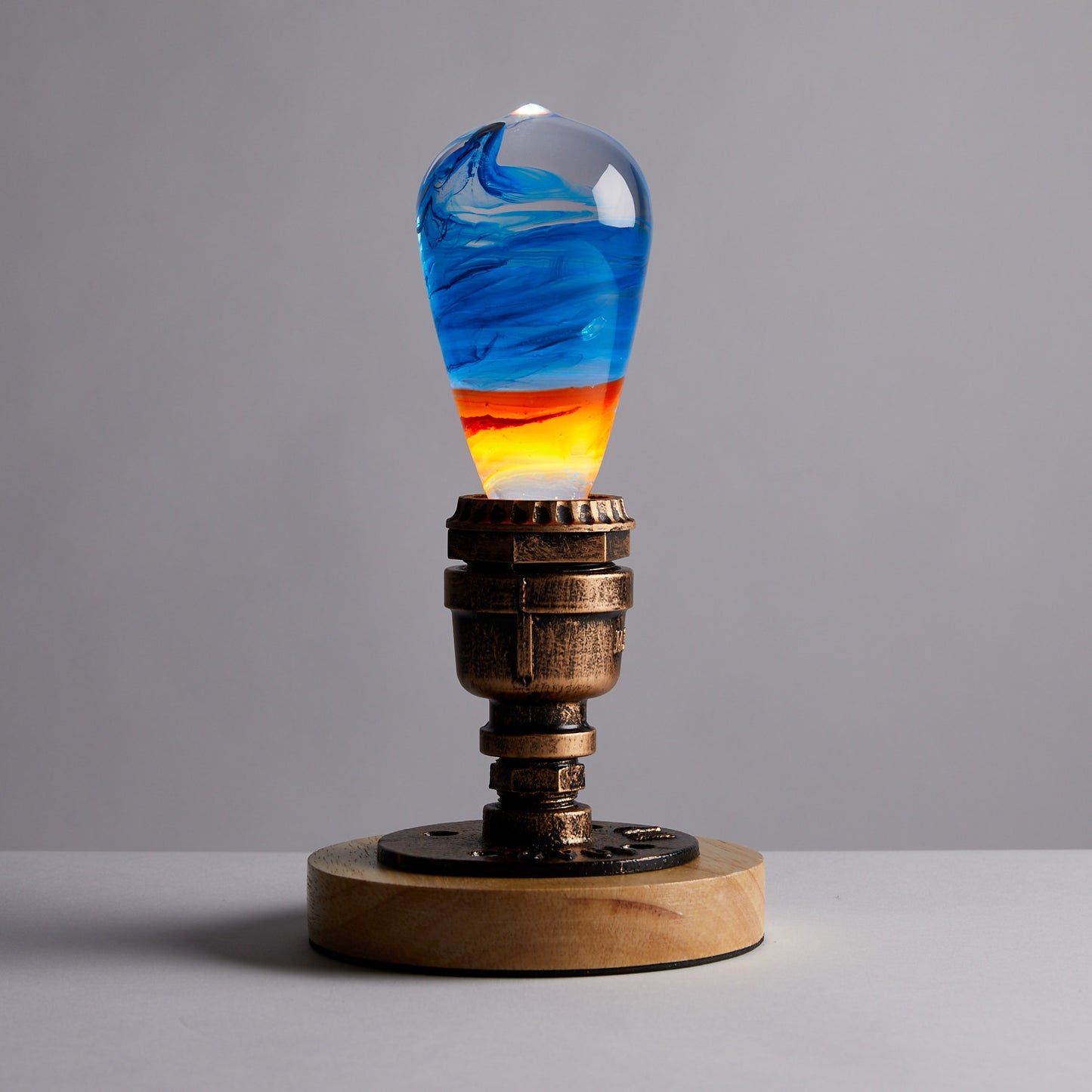 Clear lightbulb glowing from within, filled with yellow, orange, red, and blue swirls, set in vintage copper and wood base.