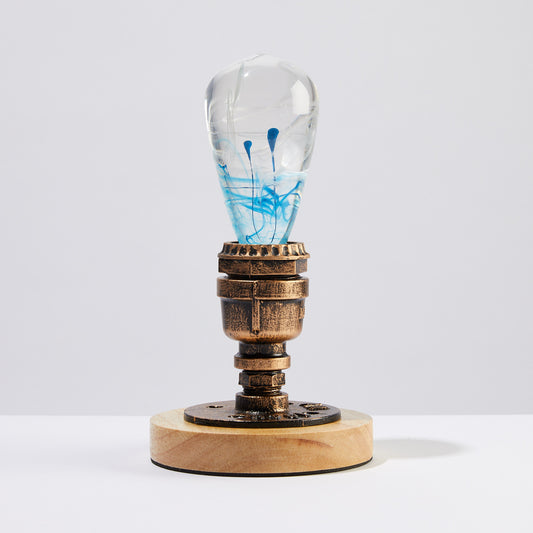 Decorative light bulb with blue and white ink drop swirl inside, screwed into a vintage style brass and wood base.