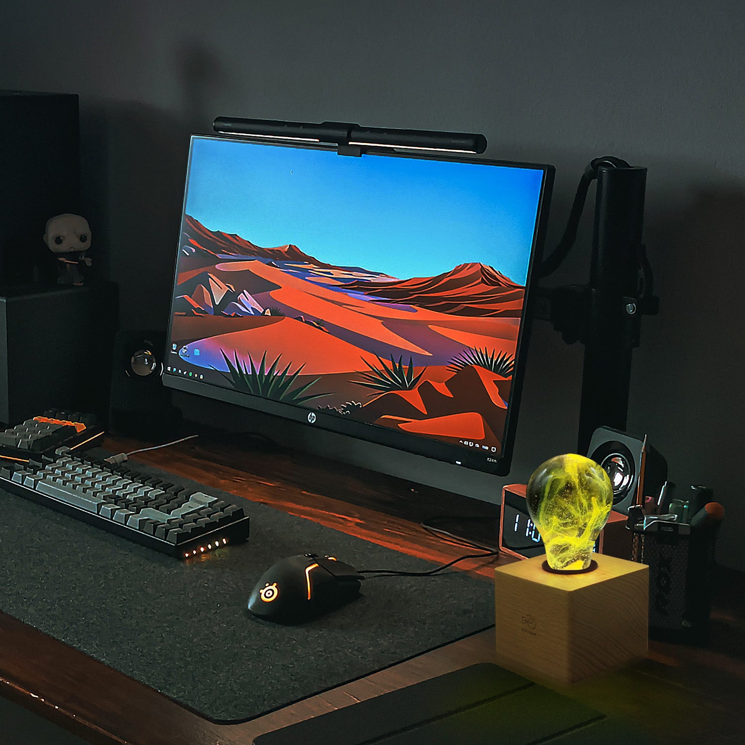 Clear lightbulb filled with yellow nebula clouds set in wooden base on top of desk beside clock and computer terminal.