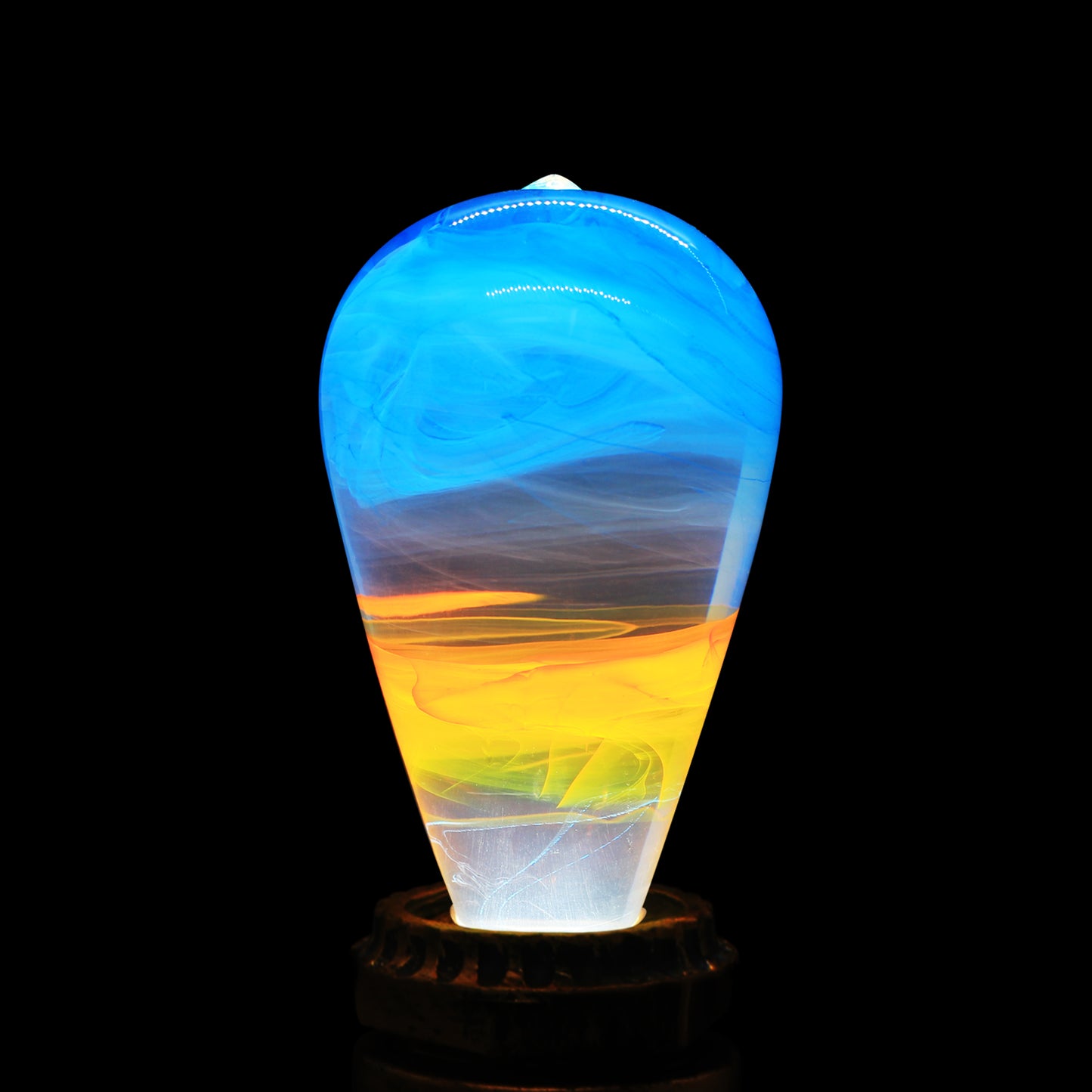 Illuminated clear lightbulb filled with yellow and blue swirls set in vintage copper colored base.