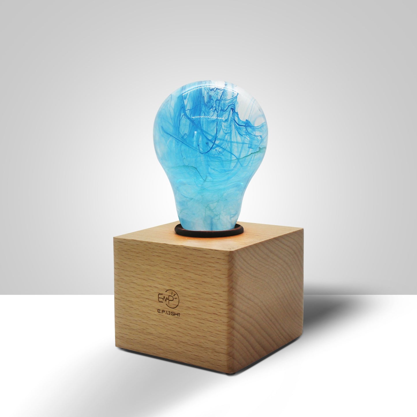 Clear lightbulb filled with blue swirls, in wooden base atop on white surface in brightly lit room.