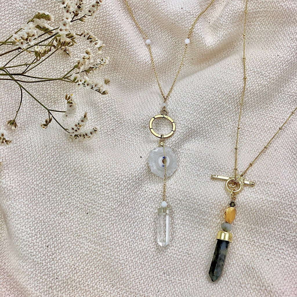 Solar quartz necklace shown on a cloth background, next to Lariat style necklace with large labradorite pendant.